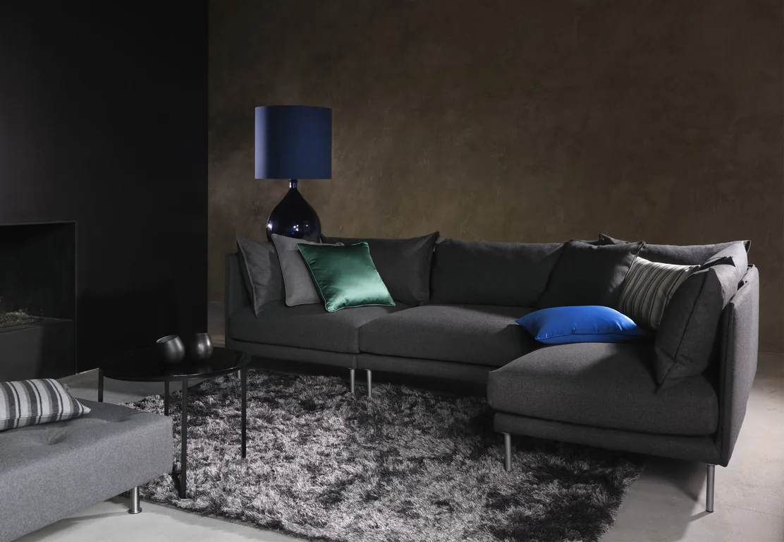 Wohnraum mit grauem Sofa, Kissen in Grün und Blau und dunkler Wand